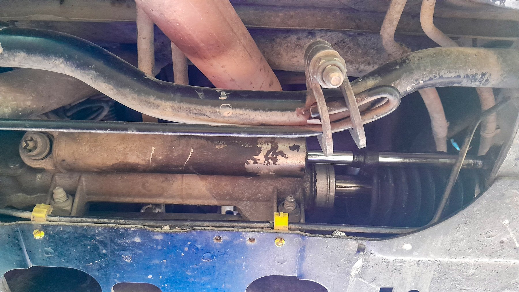 The hydraulic steering of a 2005 Citroën C15, photographed from underneath: a plain rack with an external assist cylinder bolted alongside it and hydraulic lines feeding each end.