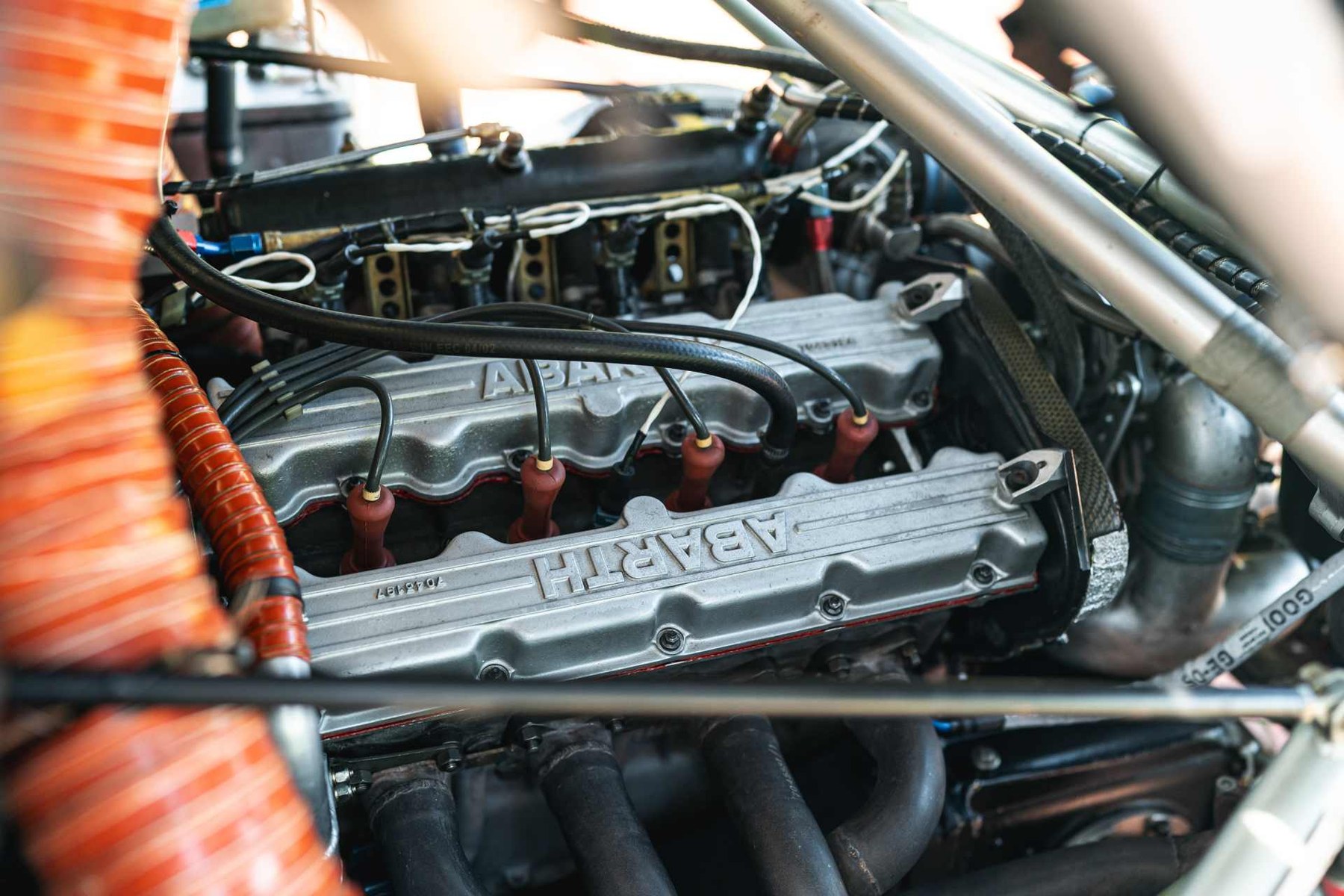 The reason the S4 mattered: a 1,759cc four with ABARTH cast into both cam covers, fed by a supercharger and a turbocharger at the same time. The orange ducting at the left of the frame is part of the plumbing that made the idea work.