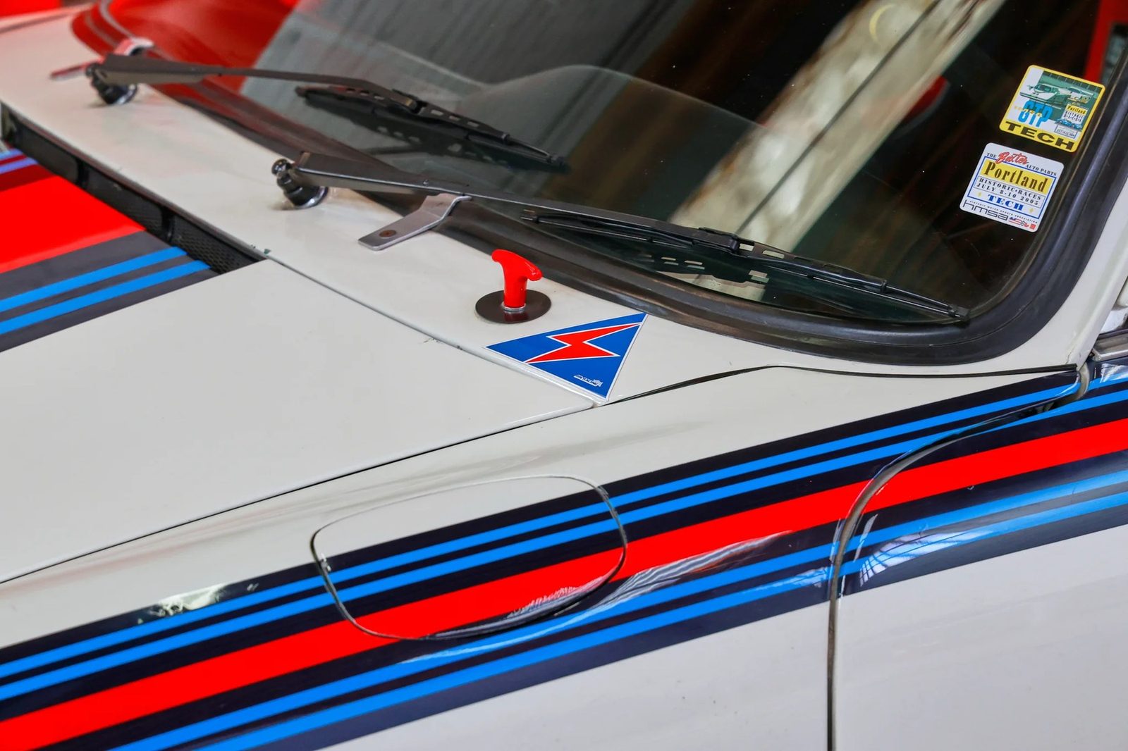 A tech-inspection sticker from the Portland Historic Races, dated July 2005, still stuck to the windshield — one of several period race decals documenting the car's decades of vintage competition.