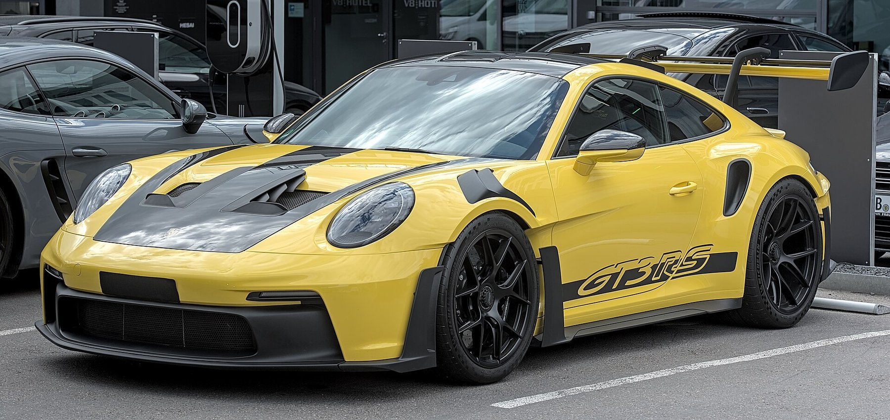 A 992-generation Porsche 911 GT3 RS. The rear wing hangs from swan-neck supports so the uninterrupted low-pressure surface faces downward, and Porsche states this is the first series-production 911 whose wing sits higher than the roofline — putting it above the air the roof has already disturbed.