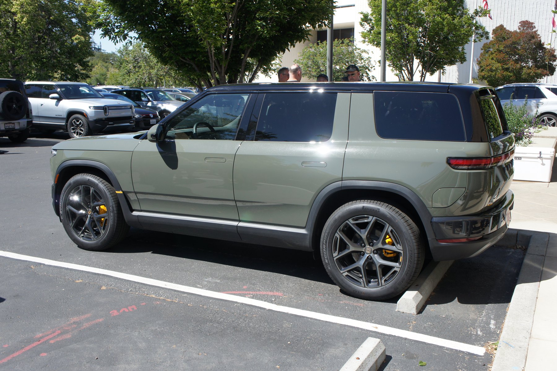 The R2 from the side. Yellow calipers and 21-inch wheels mark this as a Performance car — the only trim anyone outside Rivian has driven. Note the R1S parked behind it for scale.