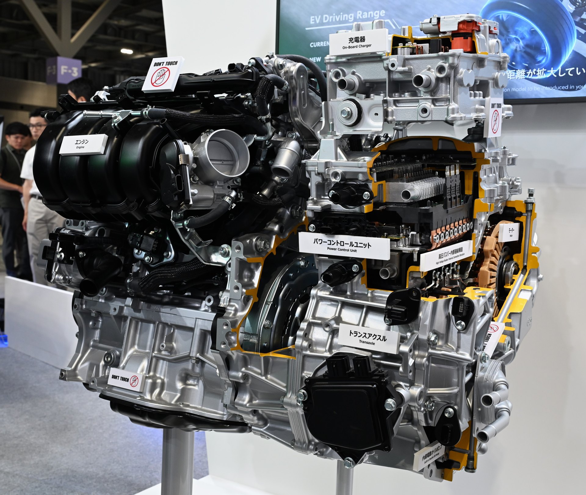 A cutaway of the plug-in hybrid system used in the 2026 RAV4, displayed with its power control unit, on-board charger and transaxle labelled. The recall is not about any of this hardware — it is about the software that initialises the motors inside it.